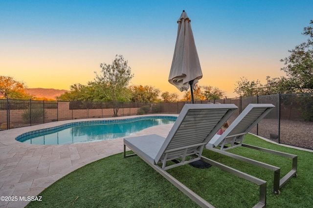 pool at dusk featuring a lawn, a fenced in pool, and a fenced backyard