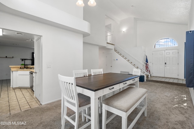 dining area featuring visible vents, light colored carpet, stairway, high vaulted ceiling, and light tile patterned flooring