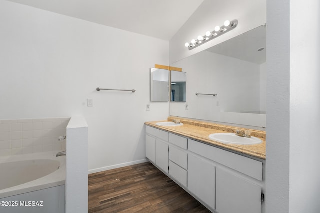 full bathroom with double vanity, a sink, a bath, and wood finished floors