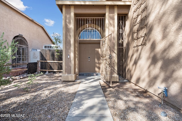 doorway to property with stucco siding, a gate, and fence