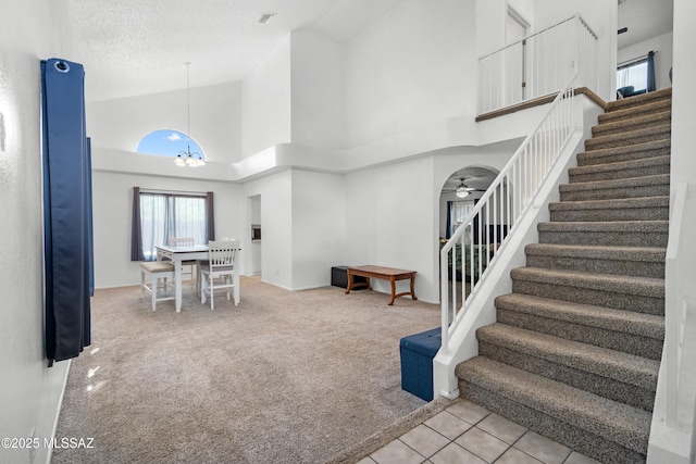 stairs with carpet floors, ceiling fan with notable chandelier, high vaulted ceiling, and a textured ceiling