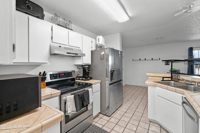 kitchen with appliances with stainless steel finishes, light tile patterned floors, white cabinets, tile counters, and under cabinet range hood