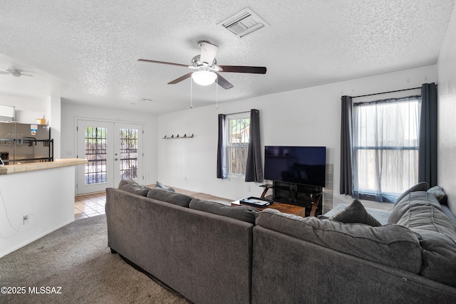 living room with french doors, a ceiling fan, a textured ceiling, visible vents, and light carpet