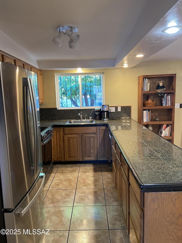 kitchen featuring freestanding refrigerator, a peninsula, electric stove, brown cabinets, and a sink