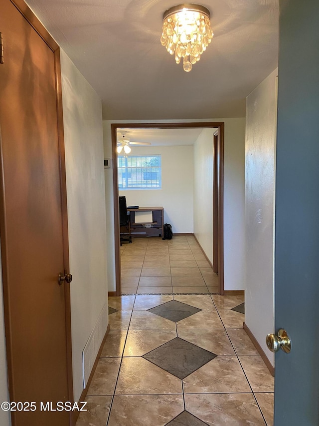 hallway with visible vents, baseboards, tile patterned floors, and an inviting chandelier