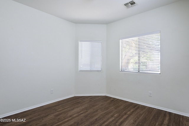 empty room featuring visible vents, dark wood finished floors, and baseboards