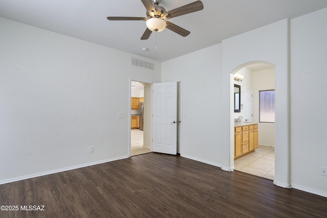 unfurnished bedroom featuring visible vents, arched walkways, wood finished floors, baseboards, and freestanding refrigerator
