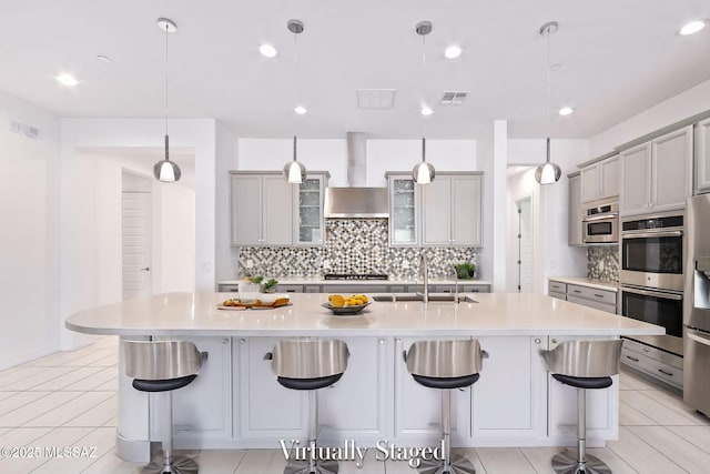 kitchen featuring visible vents, decorative backsplash, wall chimney exhaust hood, gray cabinets, and a sink