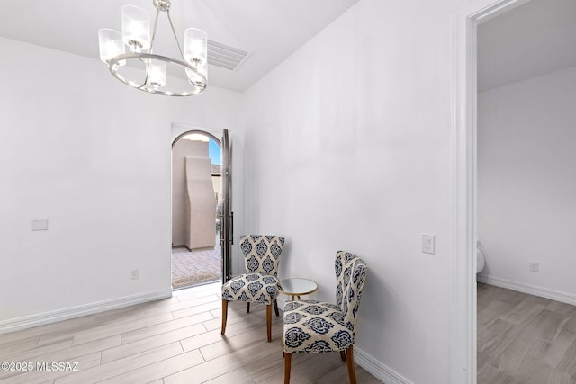sitting room with arched walkways, baseboards, a chandelier, and light wood-style floors
