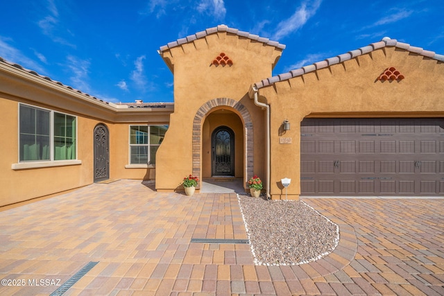 doorway to property with a tiled roof, a garage, and stucco siding