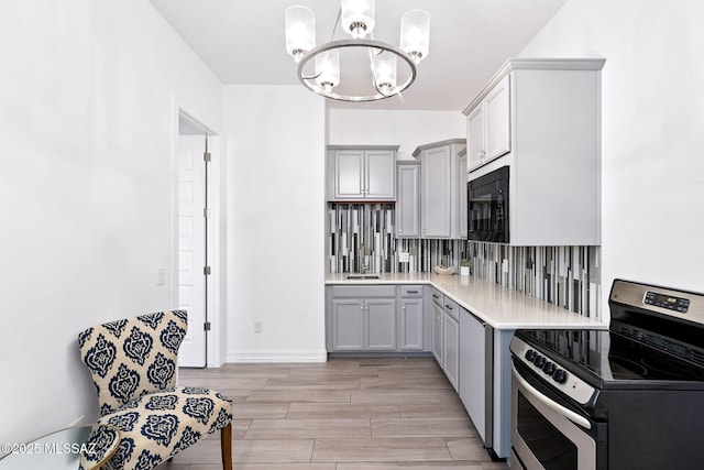 kitchen featuring stainless steel range with electric stovetop, black microwave, light countertops, a sink, and a notable chandelier