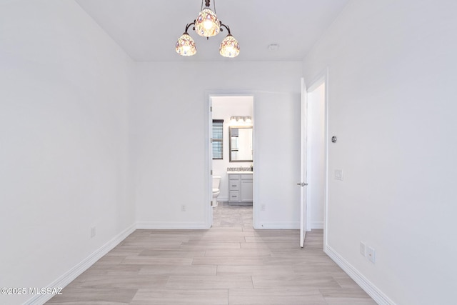 empty room featuring baseboards, a chandelier, and light wood-type flooring