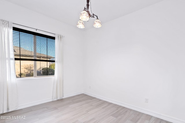 unfurnished room with baseboards, a chandelier, and light wood-style floors