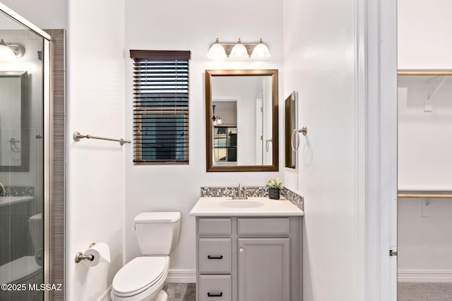 bathroom featuring toilet, a shower stall, a walk in closet, and vanity