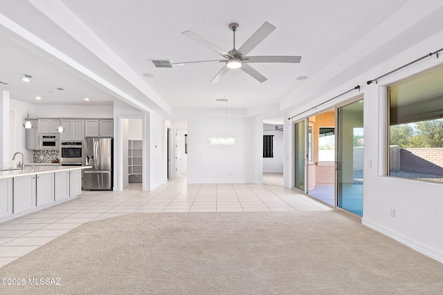 unfurnished living room with visible vents, light tile patterned flooring, light colored carpet, a sink, and ceiling fan with notable chandelier