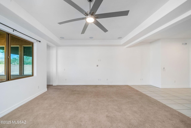 unfurnished room featuring a raised ceiling, ceiling fan, light tile patterned floors, and light carpet