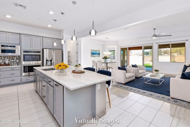 kitchen with gray cabinets, a kitchen breakfast bar, a sink, open floor plan, and stainless steel appliances