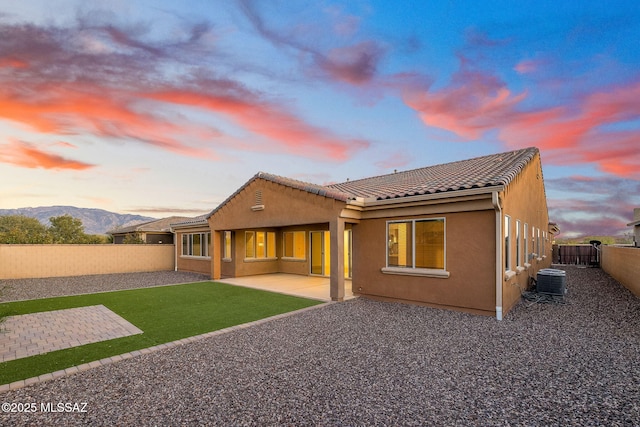back of property at dusk with a tile roof, cooling unit, a fenced backyard, a patio, and stucco siding