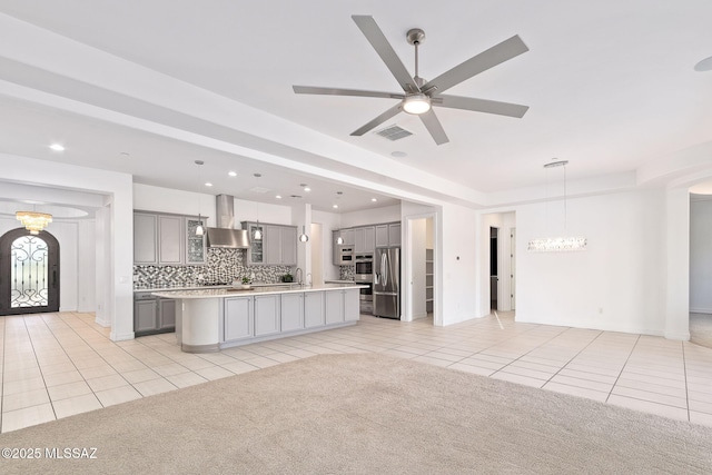 kitchen with light tile patterned flooring, appliances with stainless steel finishes, gray cabinets, wall chimney exhaust hood, and open floor plan