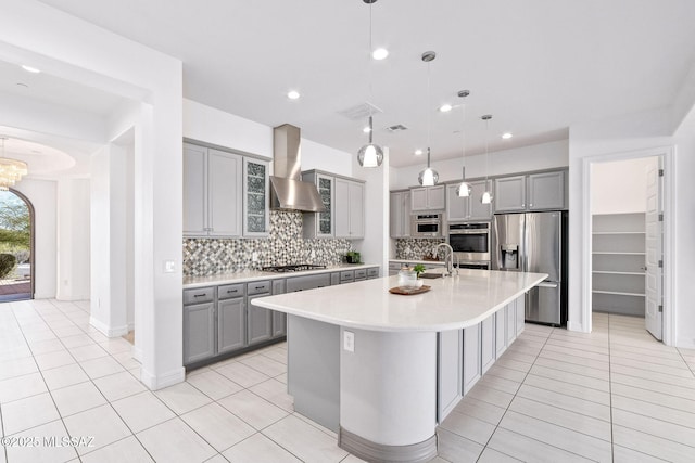 kitchen with wall chimney range hood, stainless steel appliances, gray cabinetry, and light tile patterned flooring