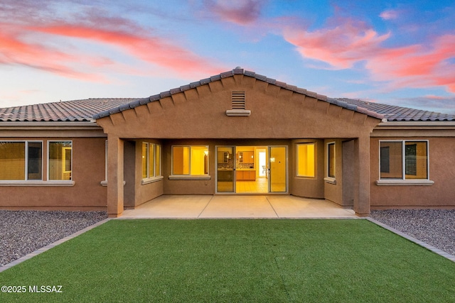rear view of property featuring a patio, stucco siding, a yard, and a tile roof