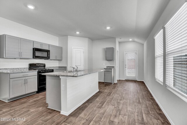 kitchen featuring a wealth of natural light, light stone counters, a sink, black appliances, and gray cabinetry