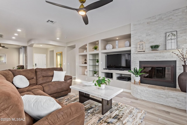living area with visible vents, wood finished floors, a stone fireplace, built in shelves, and a ceiling fan
