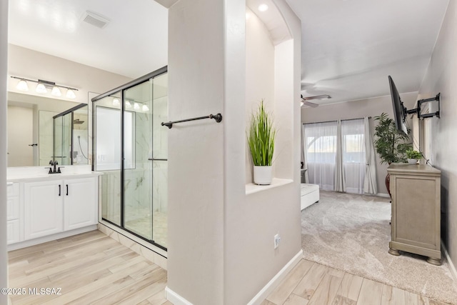 bathroom with visible vents, wood finished floors, baseboards, vanity, and a marble finish shower