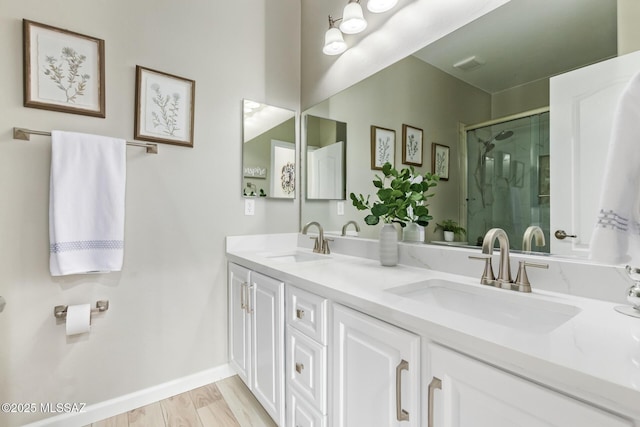full bath with double vanity, a shower stall, a sink, and wood finished floors