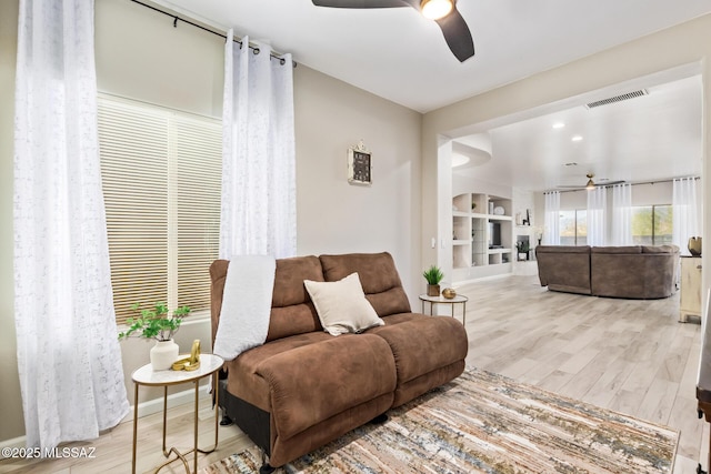 living room featuring built in shelves, a ceiling fan, baseboards, wood finished floors, and visible vents