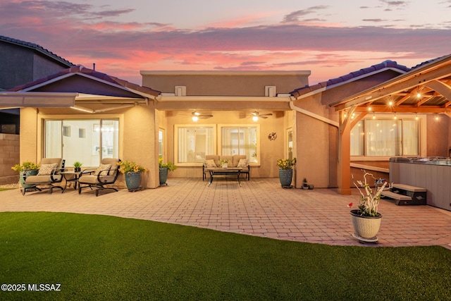 rear view of property with a hot tub, a patio, a tiled roof, and stucco siding