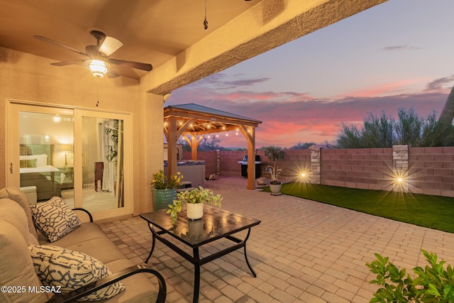 patio terrace at dusk featuring a fenced backyard, a ceiling fan, a hot tub, and a grill