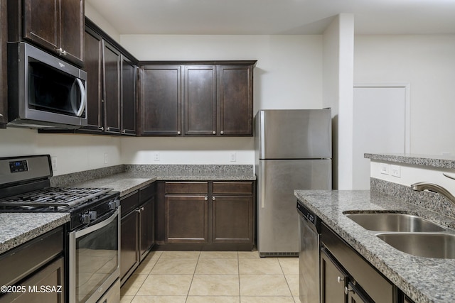 kitchen featuring appliances with stainless steel finishes, a sink, light tile patterned floors, and dark brown cabinetry