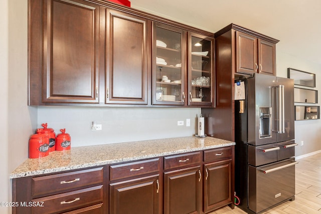 kitchen with light wood-type flooring, glass insert cabinets, light stone counters, and high end fridge