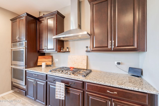 kitchen with wall chimney range hood, light stone counters, appliances with stainless steel finishes, and dark brown cabinetry
