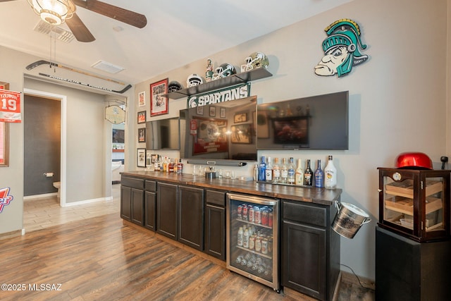 bar with wine cooler, a bar, a ceiling fan, and wood finished floors