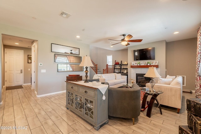 living area featuring stairs, visible vents, a fireplace, ceiling fan, and wood tiled floor