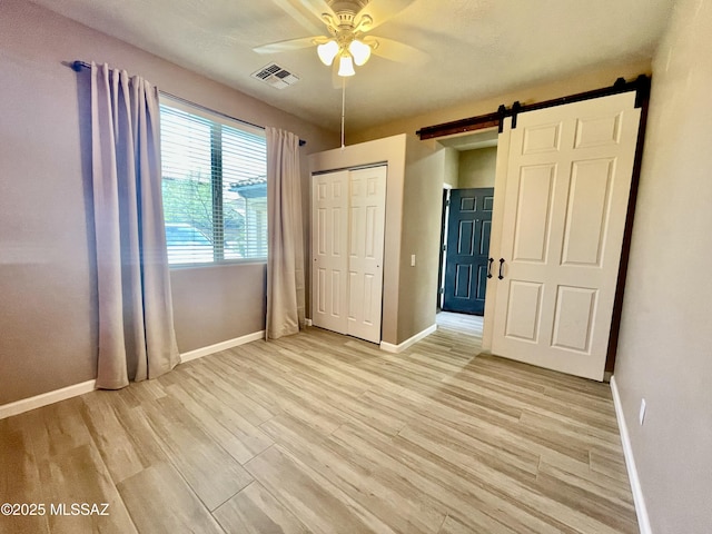 unfurnished bedroom featuring light wood finished floors, visible vents, a barn door, and baseboards