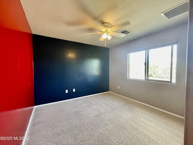carpeted spare room with visible vents, baseboards, and a ceiling fan