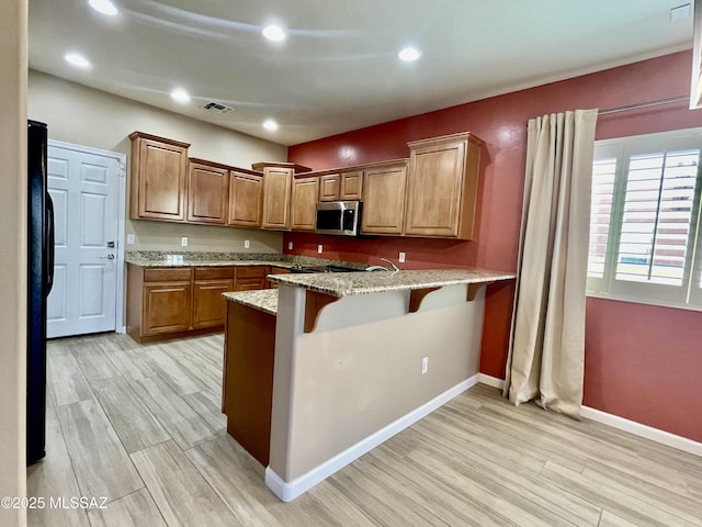 kitchen featuring a peninsula, light wood-type flooring, visible vents, stainless steel microwave, and light stone counters