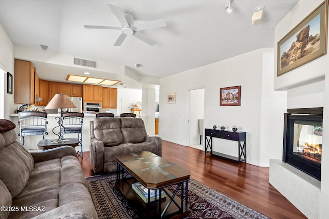 living room featuring a multi sided fireplace, a ceiling fan, dark wood-type flooring, and visible vents