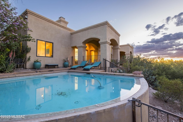 4519 N Camino Kino, Tucson, AZ 85718 - back of property at dusk with an outdoor pool, stucco siding, and a chimney
