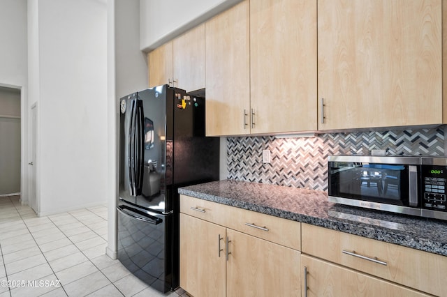 kitchen with freestanding refrigerator, stainless steel microwave, and light brown cabinetry