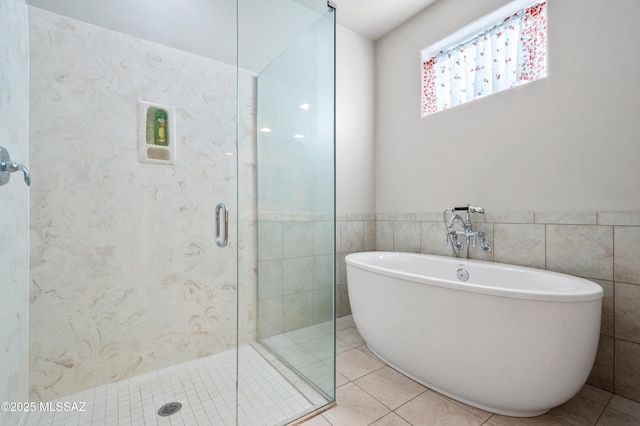 bathroom featuring tile patterned flooring, tile walls, a wainscoted wall, a freestanding bath, and a shower stall
