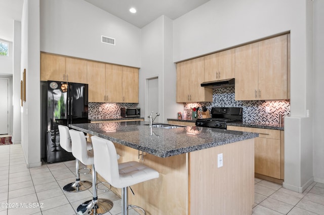 kitchen with light brown cabinets, a high ceiling, under cabinet range hood, a sink, and black appliances