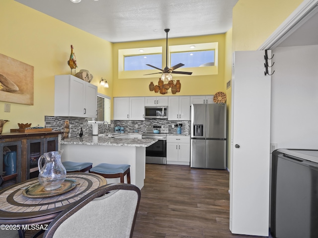 kitchen with ceiling fan, stainless steel appliances, white cabinetry, a peninsula, and decorative backsplash