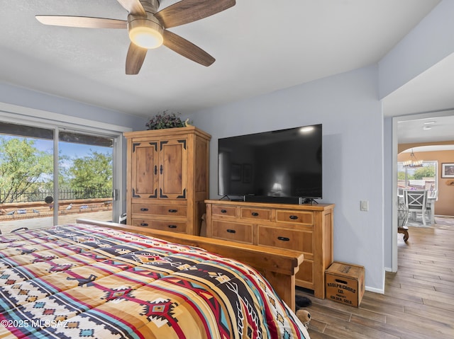 bedroom with baseboards, access to outside, ceiling fan with notable chandelier, and wood finished floors