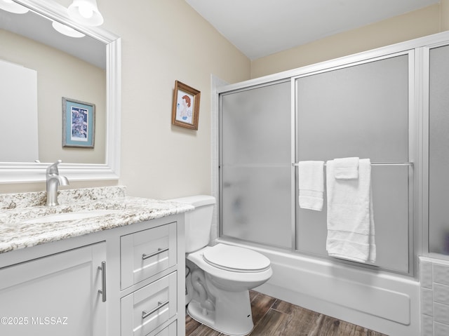 full bath featuring vanity, combined bath / shower with glass door, wood finished floors, and toilet