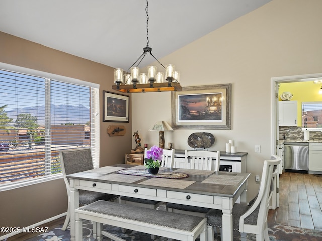 dining room with a healthy amount of sunlight, vaulted ceiling, wood finished floors, and a notable chandelier