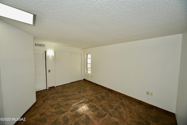 empty room with stone finish floor, a textured ceiling, visible vents, and baseboards